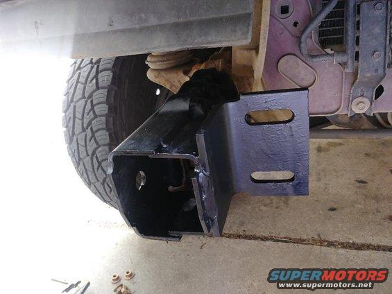 close-up of a new black metal bumper bracket being installed on a vehicle's frame near the tire