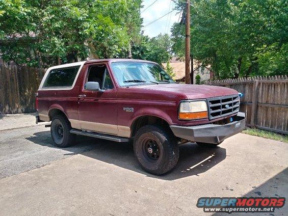 Maroon Ford Bronco with tan lower body trim and a white roof. It has an aftermarket bumper