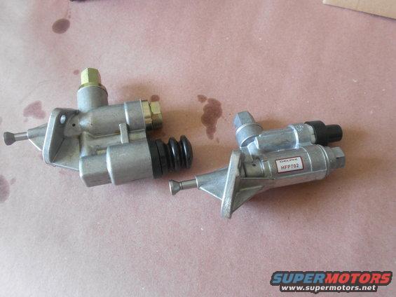 Two silver fuel pumps with black rubber bellows and brass fittings on a brown surface