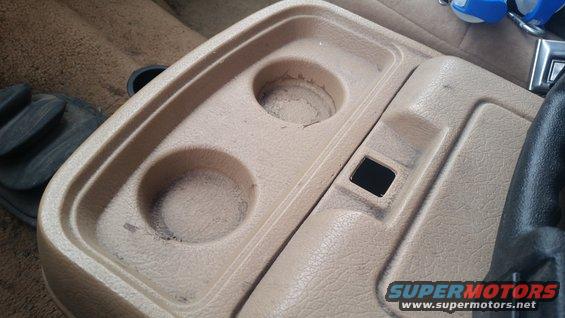 Tan center console with two cup holders and a small storage compartment
