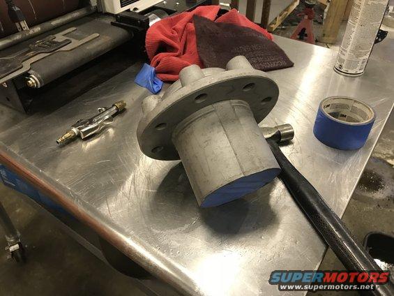 Metal automotive part with bolt holes, hammer, tape, and air tool on a workbench