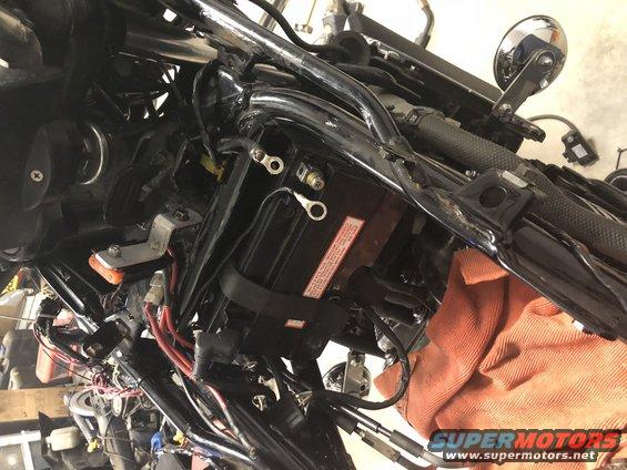 motorcycle battery with red and black wires connected, orange cloth nearby