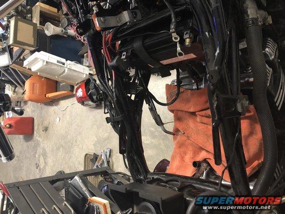 Motorcycle wiring harness and battery area, with tools and gas can in background