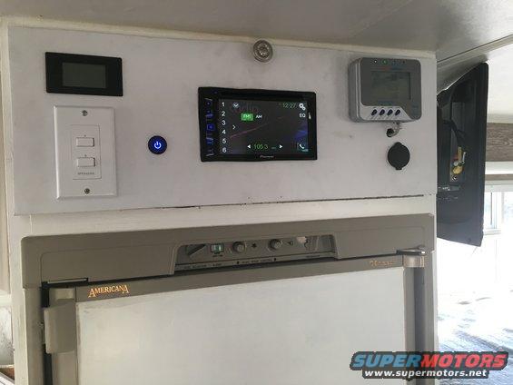 RV control panel with digital display, switches, power button, Pioneer stereo, and a solar charge controller above an Americana refrigerator