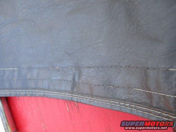 Close-up of stitching on a dark-colored vehicle soft top, with a red surface visible underneath