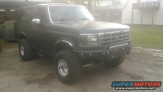 Dark gray 1992 Ford Bronco with aftermarket bumper and LED light bar, lifted on large tires