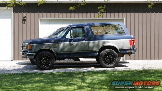 1987 Ford Bronco parked in front of a garage, another vehicle partially visible behind it