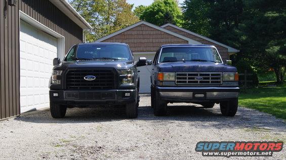 Front view of a black Ford F-150 next to an older blue Ford truck