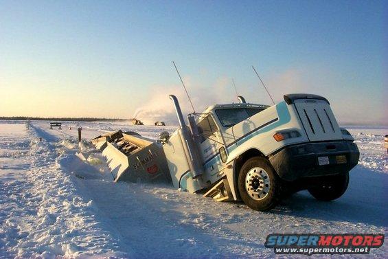 Semi-truck stuck in snow, with snowplows in background