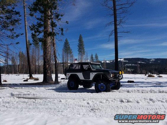 Modified Ford Bronco driving in snow with trees and mountains in background