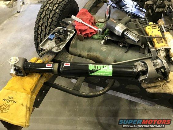 Black driveshaft with green Oliver's Drive Shaft label, held by yellow glove