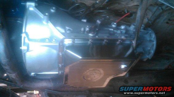 Underside view of a transmission pan with a circular emblem and a torque converter