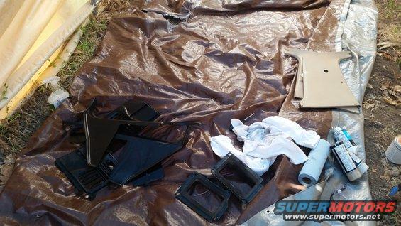 Car interior trim pieces and a pillar cover laid out on tarps, with spray paint cans nearby