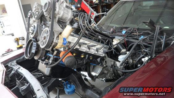 Maroon vehicle engine bay with engine hoist and engine components.