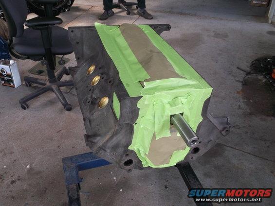 Engine block masked with green tape and brown paper, with a metal rod inserted