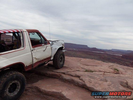 White and red Ford Bronco parked on a rock ledge overlooking a canyon
