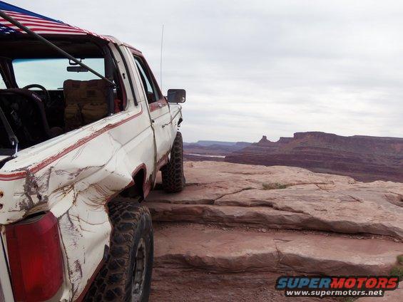 White Ford Bronco with red stripe, dented rear quarter panel, parked on rocky overlook
