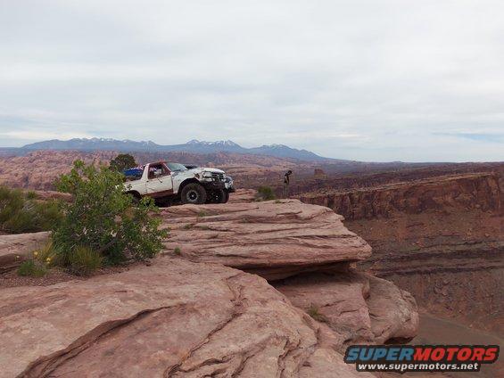 White Ford Bronco with red top on a cliff edge, front 3/4 view, damaged front end