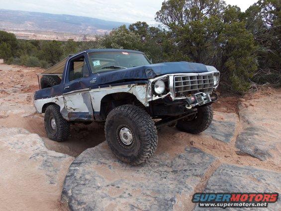 Modified Ford Bronco off-roading on large rocks, front end damaged, winch installed