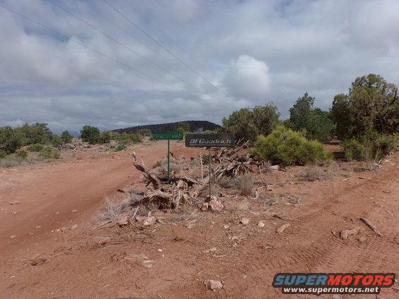 Dirt road in a dry, scrubby area with signs for 'GRIZZLY DAY' and 'BFGoodrich'. Power lines overhead