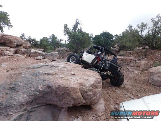 Black off-road buggy with a roll cage climbing over rocks on a dirt trail