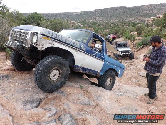 Blue and white Ford Bronco with 'Faded Glory' on the side, navigating a rocky trail with other vehicles behind it