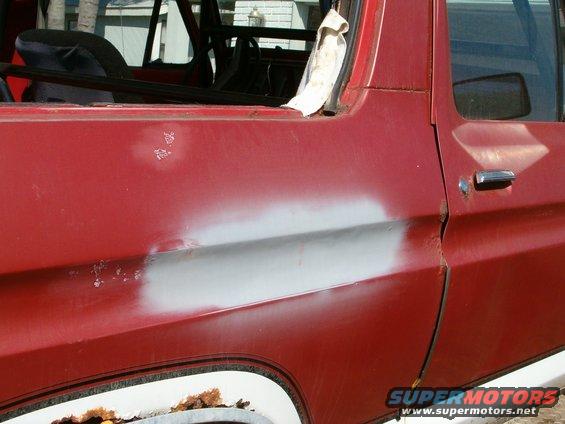 Red vehicle door with a patch of body filler and some rust spots. Interior roll cage visible