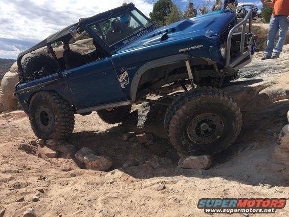 Blue 1984 Ford Bronco with off-road modifications navigating rocky terrain