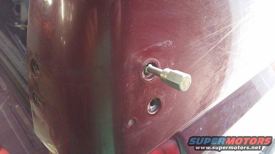 Maroon car body panel with a hex bolt inserted into a hole, showing two other screw holes nearby