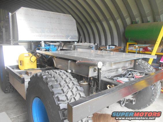 Custom truck chassis with large aluminum cargo bed, yellow fuel can, and large off-road tires. Supermotors.net logo visible