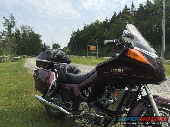 Maroon touring motorcycle parked on a gravel road next to a picnic area