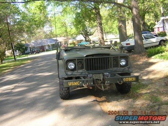 Green military truck with USMC marking on front bumper and license plate 809131. White car parked in background