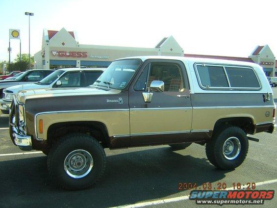 Side view of a brown and tan two-tone SUV parked in a lot. Another car is visible behind it
