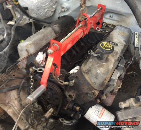 Engine assembly with red engine hoist, oil filter, and chains. Visible text includes "SUPERMOTORS.NET"