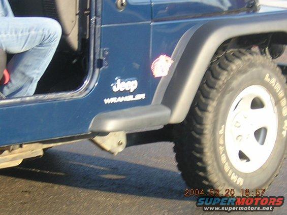 Blue Jeep Wrangler side view, showing door, fender flare, and tire. A person's legs are visible inside