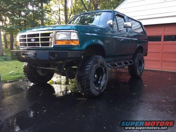 Green 1996 Ford Bronco with aftermarket bumper and large tires parked in front of a garage