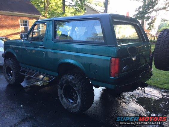 Green Ford Bronco with aftermarket wheels and tires, side steps, and a rear-mounted spare tire