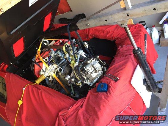 Engine bay covered in red cloth with engine removed and suspended by a hoist