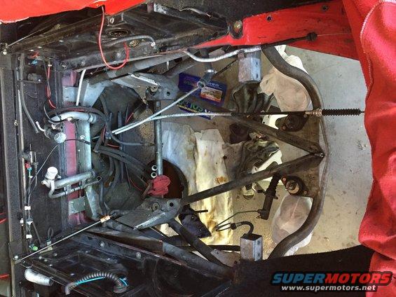 Red car engine bay with exposed mechanical components, hoses, and wiring. A blue box is visible
