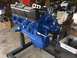 1969 Ford Mustang - A blue V8 engine with black valve covers labeled "COBRA LE MANS" is mounted on an engine stand in a workshop.