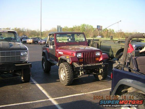 Red Jeep Wrangler YJ parked in a lot with other vehicles. Date stamp shows 2004
