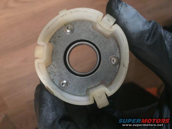 Hand holding a white plastic housing with a metal plate secured by three screws