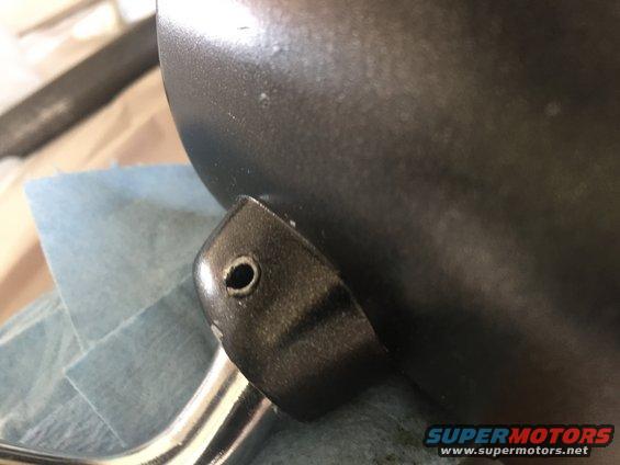Close-up of a dark metal engine part mounting bracket with a single bolt hole
