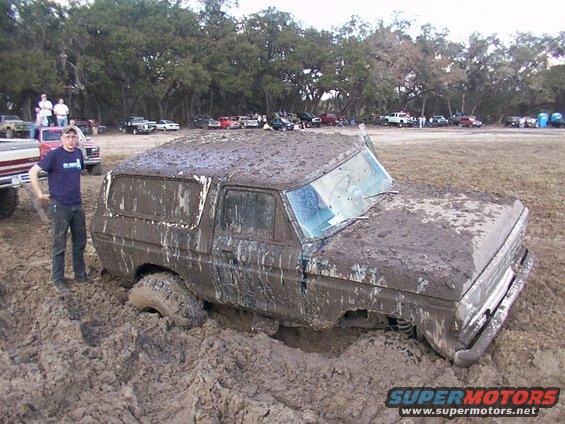 Mud-covered 1978 Ford Bronco stuck in mud pit with a person standing next to it