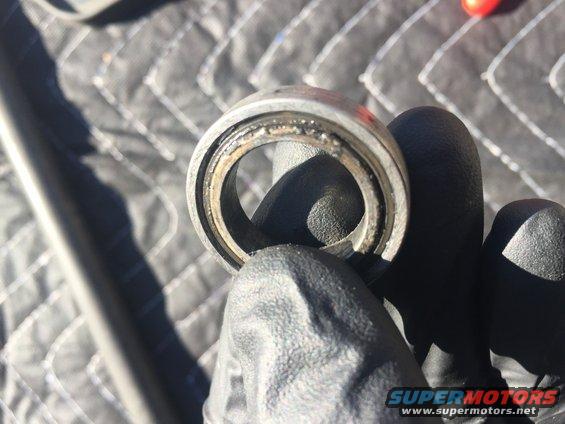 Gloved hand holding a worn wheel bearing with visible damage
