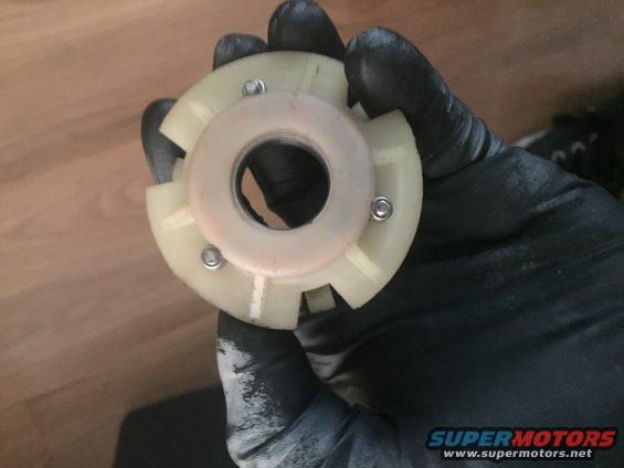 Gloved hand holding a white plastic steering column bearing retainer with metal screws