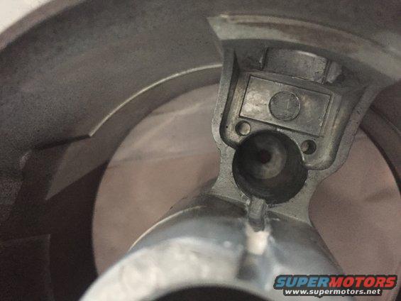 Close-up of a metal steering column part with a circular opening and a rectangular recess containing a coin