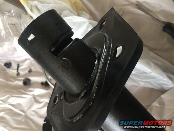 Black metal steering column component with mounting bracket. Small parts and a screwdriver are visible in the background