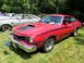 1971 Ford Ranchero - A red coupe with a prominent hood scoop and side stripes is displayed at an outdoor event.