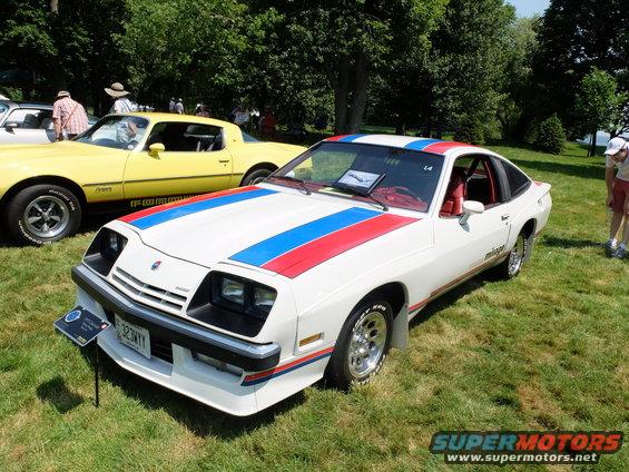 White 1977 Pontiac Firebird Trans Am with red and blue racing stripes, parked on grass